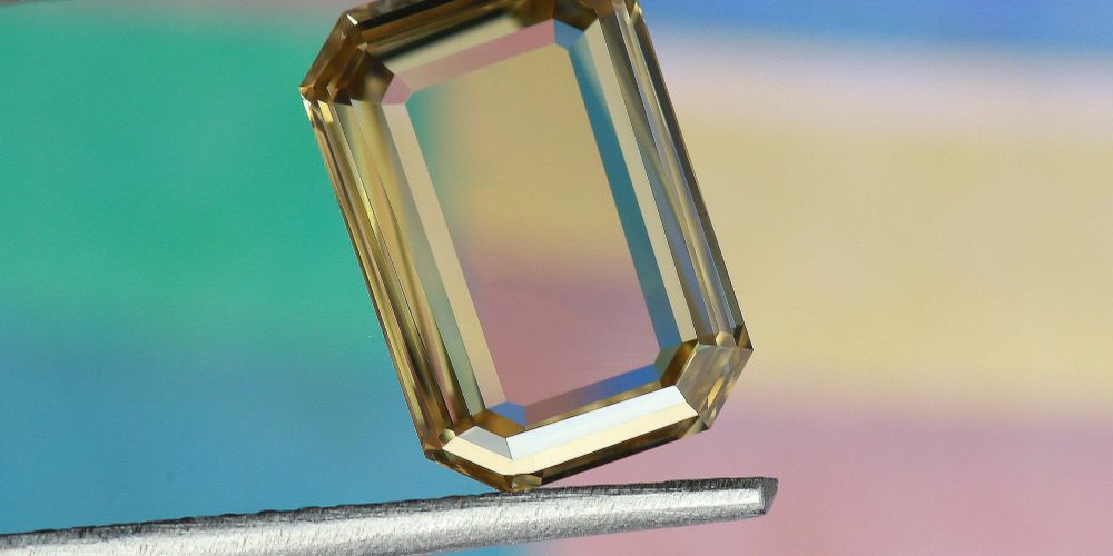 A luxurious octagonal gemstone held by tweezers, showcasing its clear facets and shine.